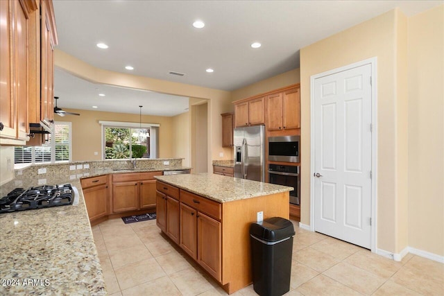 kitchen featuring light stone counters, appliances with stainless steel finishes, light tile patterned floors, decorative light fixtures, and a center island