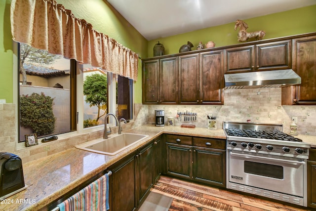 kitchen with decorative backsplash, dark brown cabinetry, sink, light stone countertops, and designer range