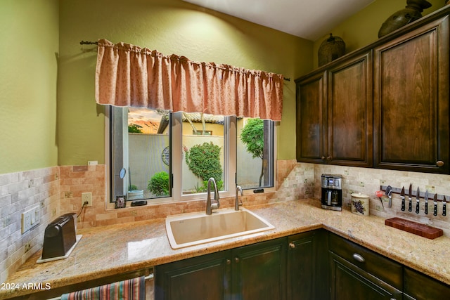 kitchen featuring backsplash, light stone counters, sink, and dark brown cabinets