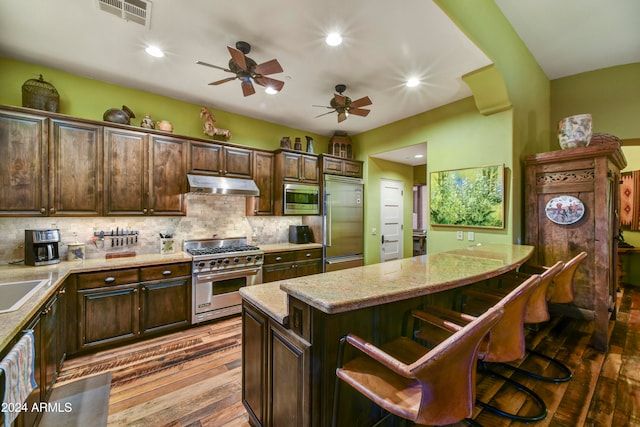 kitchen with light hardwood / wood-style floors, built in appliances, dark brown cabinetry, a kitchen breakfast bar, and a kitchen island