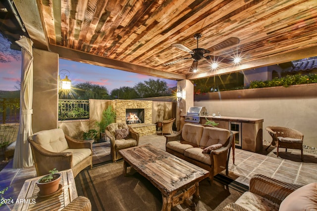 patio terrace at dusk featuring ceiling fan, area for grilling, and an outdoor living space with a fireplace