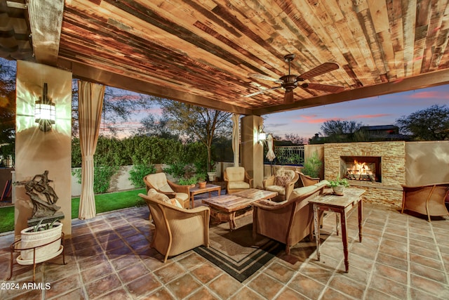 patio terrace at dusk with an outdoor living space with a fireplace and ceiling fan