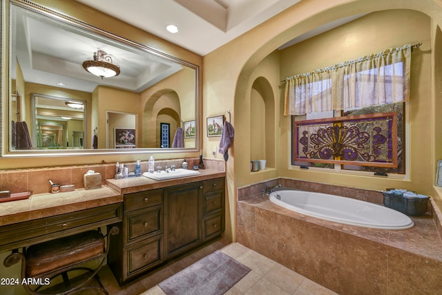 bathroom featuring a relaxing tiled tub, vanity, tile patterned floors, and a tray ceiling