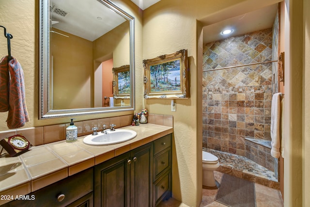 bathroom featuring tiled shower, tile patterned flooring, vanity, and toilet