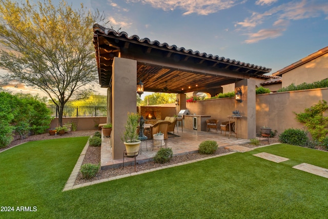 patio terrace at dusk with exterior bar, a lawn, area for grilling, and a grill