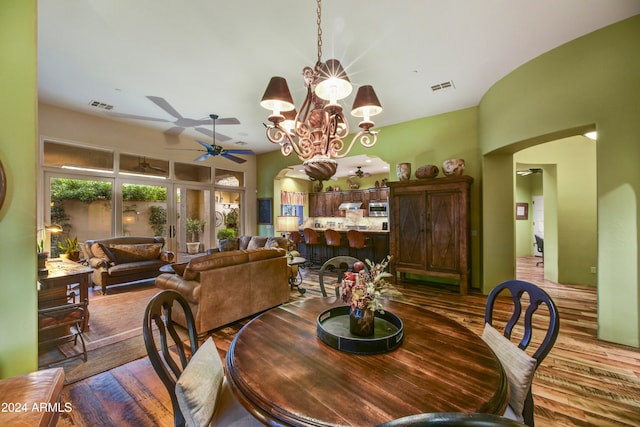 dining room featuring ceiling fan with notable chandelier, wood-type flooring, and vaulted ceiling