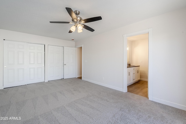 unfurnished bedroom with light carpet, connected bathroom, multiple closets, and ceiling fan