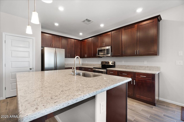 kitchen with wood finish floors, visible vents, a sink, light stone counters, and appliances with stainless steel finishes