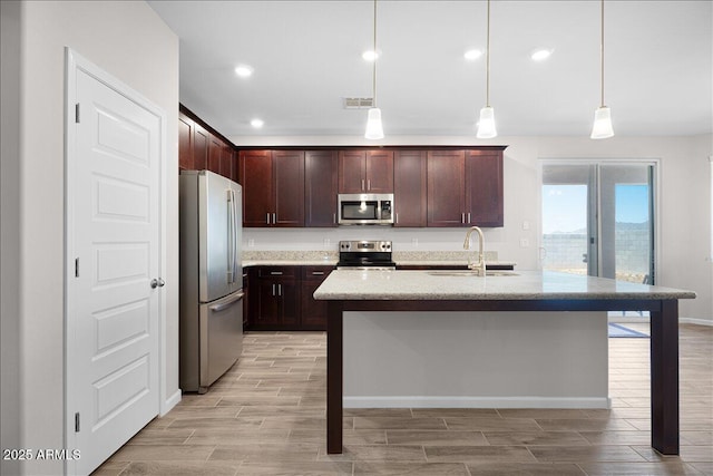 kitchen featuring visible vents, a sink, stainless steel appliances, wood tiled floor, and hanging light fixtures