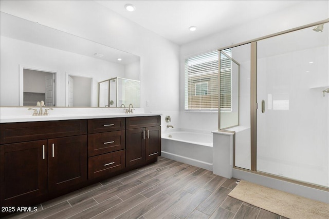 full bathroom featuring a shower stall, wood tiled floor, a garden tub, double vanity, and a sink
