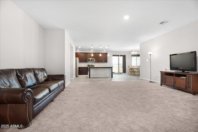 living room with a chandelier, visible vents, light colored carpet, and baseboards