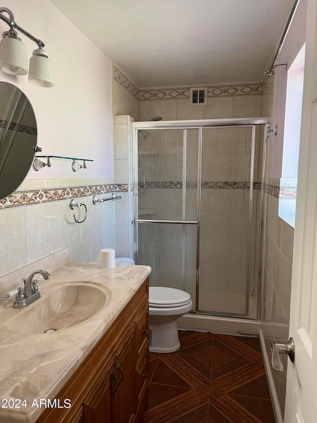 bathroom featuring tile walls, vanity, tile patterned flooring, a shower with door, and toilet