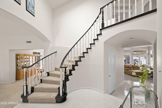 stairway with arched walkways, visible vents, baseboards, and a towering ceiling