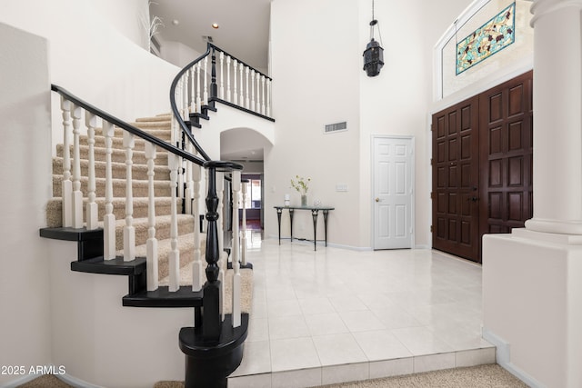 tiled foyer with visible vents, arched walkways, a high ceiling, decorative columns, and baseboards