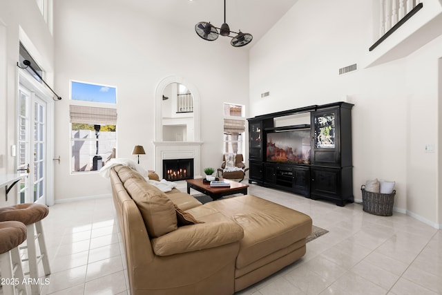 living area with light tile patterned floors, visible vents, a warm lit fireplace, and a towering ceiling