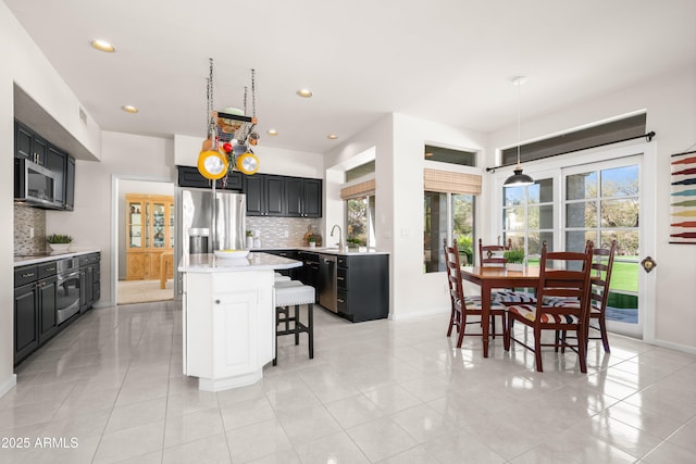 kitchen with a kitchen bar, a kitchen island, dark cabinetry, appliances with stainless steel finishes, and light countertops