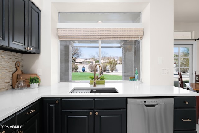 kitchen featuring tasteful backsplash, light countertops, stainless steel dishwasher, dark cabinetry, and a sink