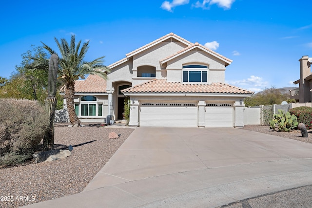 mediterranean / spanish-style home with stucco siding, a tiled roof, concrete driveway, and fence