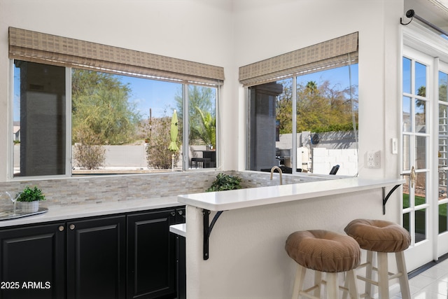 kitchen featuring a breakfast bar area, dark cabinets, decorative backsplash, and light countertops