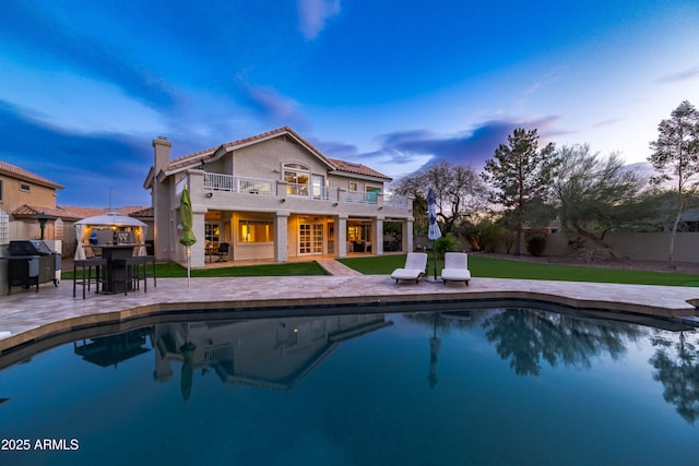 back of house featuring a balcony, a patio area, a fenced in pool, and a chimney