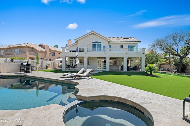 back of property featuring a balcony, a fenced backyard, a pool with connected hot tub, a patio area, and a lawn