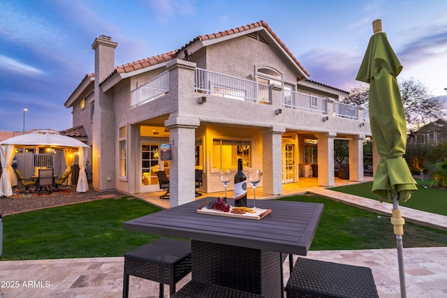 rear view of property featuring a lawn, outdoor dining space, a patio, a balcony, and a chimney