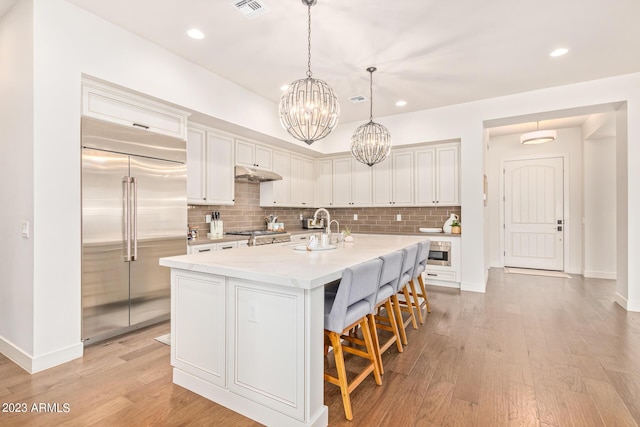 kitchen with decorative light fixtures, a breakfast bar, sink, a kitchen island with sink, and built in refrigerator