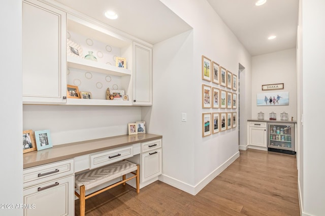 interior space featuring wine cooler, built in desk, white cabinetry, and light hardwood / wood-style floors