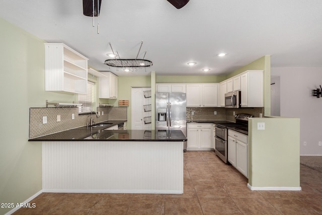 kitchen with stainless steel appliances, a peninsula, a sink, tasteful backsplash, and dark countertops