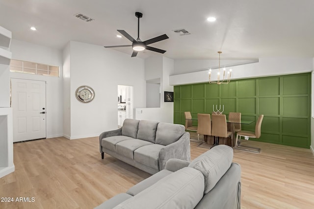 living room featuring lofted ceiling, ceiling fan with notable chandelier, and light hardwood / wood-style flooring