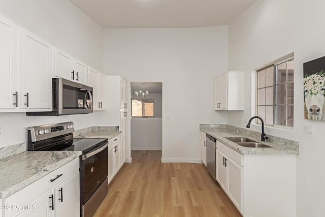 kitchen featuring white cabinetry, appliances with stainless steel finishes, a notable chandelier, light wood-type flooring, and sink