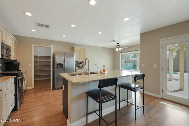 kitchen featuring stainless steel appliances, a kitchen island with sink, a breakfast bar area, ceiling fan, and sink