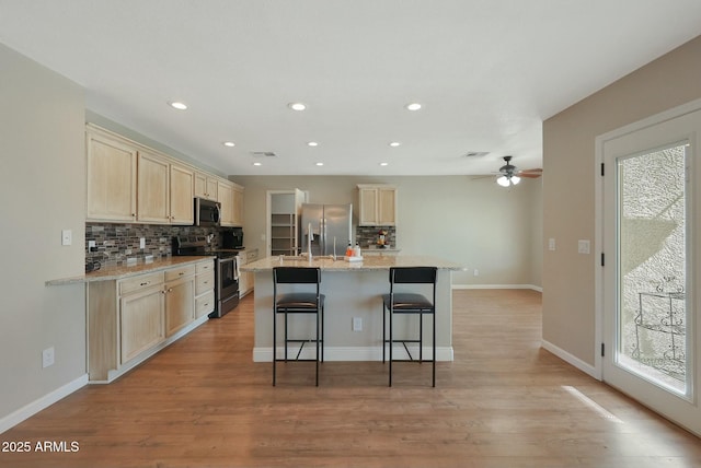 kitchen featuring stainless steel appliances, an island with sink, a kitchen bar, and light stone counters