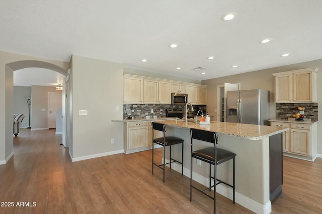 kitchen with light stone countertops, a breakfast bar, decorative backsplash, a kitchen island with sink, and appliances with stainless steel finishes