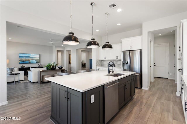 kitchen with white cabinetry, a center island with sink, stainless steel appliances, pendant lighting, and sink