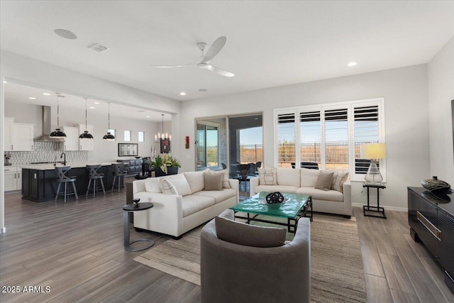 living room featuring dark wood-type flooring, ceiling fan with notable chandelier, and sink