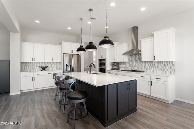 kitchen featuring wall chimney exhaust hood, pendant lighting, stainless steel appliances, and white cabinetry