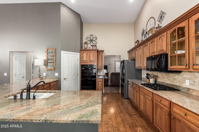 kitchen with light stone counters, dark wood-type flooring, a sink, a towering ceiling, and black appliances