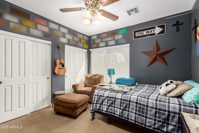 bedroom featuring carpet floors, a ceiling fan, visible vents, and two closets