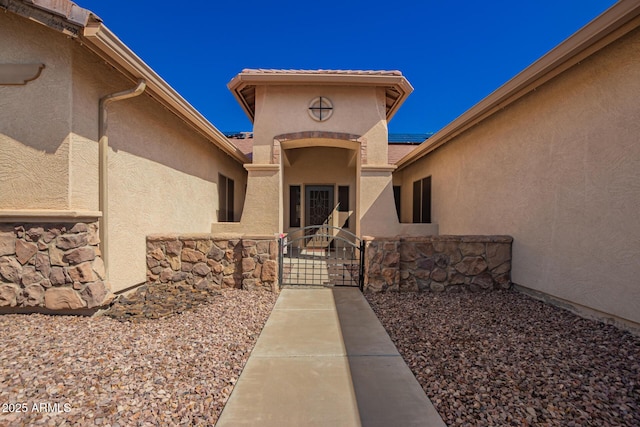 entrance to property featuring stone siding, a gate, and stucco siding