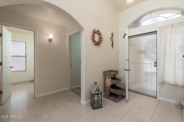 entrance foyer with arched walkways, baseboards, and light tile patterned floors