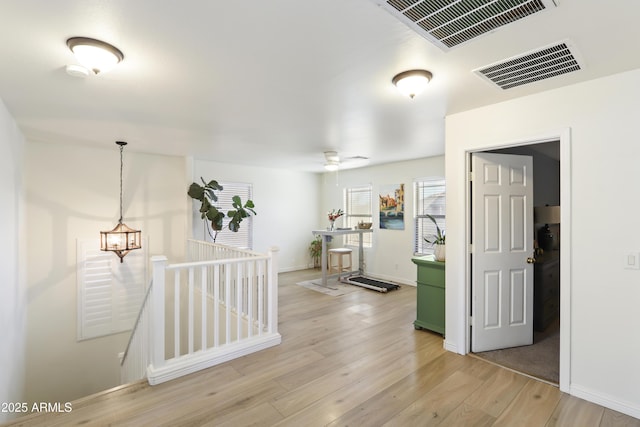 corridor featuring light wood finished floors, baseboards, visible vents, and an upstairs landing