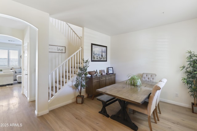 dining room featuring light wood-type flooring, baseboards, stairway, and arched walkways