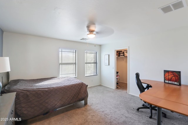 bedroom with a walk in closet, visible vents, ceiling fan, and light carpet