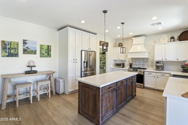 kitchen with custom exhaust hood, stainless steel appliances, light countertops, visible vents, and a kitchen island