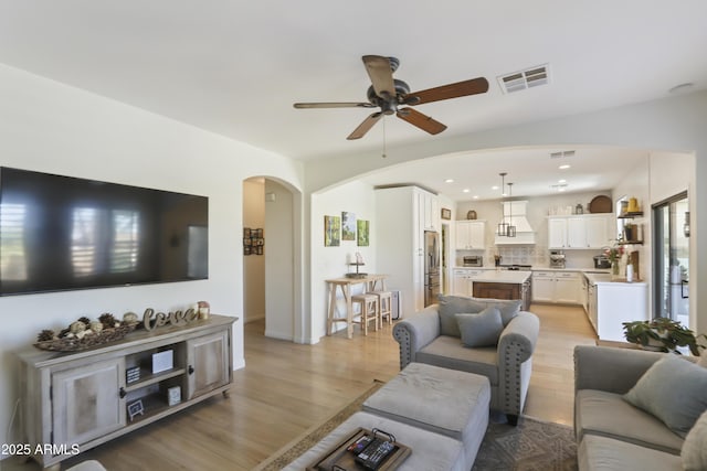 living room with arched walkways, ceiling fan, light wood-type flooring, and visible vents