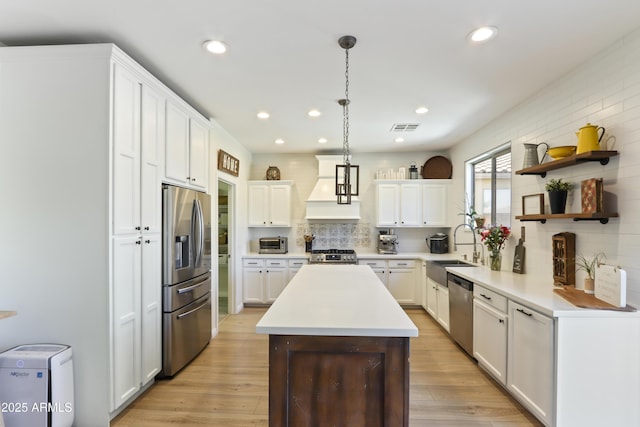 kitchen with premium range hood, light countertops, appliances with stainless steel finishes, hanging light fixtures, and open shelves