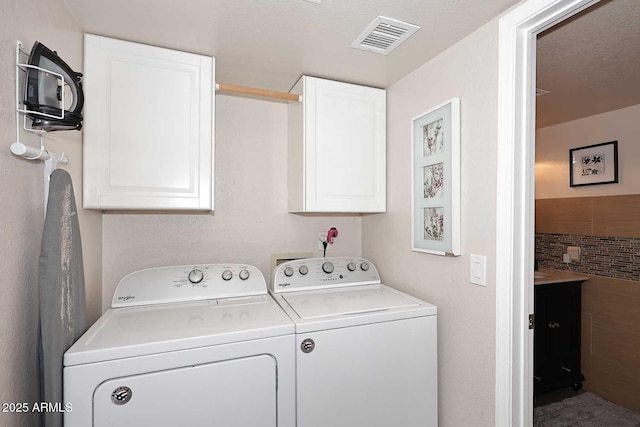 laundry room with cabinets, a textured ceiling, and washing machine and dryer