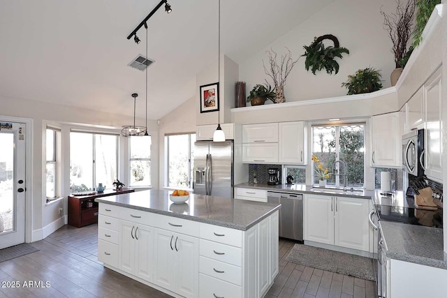 kitchen with white cabinets, appliances with stainless steel finishes, a center island, decorative backsplash, and sink