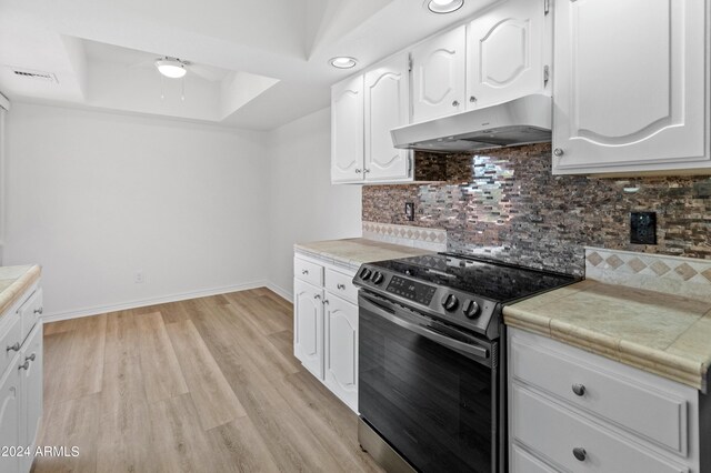 kitchen with light wood-type flooring, tasteful backsplash, tile counters, electric range oven, and a tray ceiling